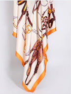 The tack print silk scarf hanging in soft folds showing the wide orange border