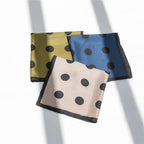 Olive, steel blue and greige dotted silk squares stacked flat in a band of window light