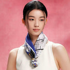 Model in a cream dress wearing the navy and gold horse print silk scarf knotted at the throat against a pink backdrop