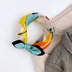 Portrait square knotted into a loop beside a beige knit and checked trousers