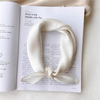 Ivory silk square knotted and set on an open magazine page to show its size