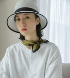 Woman in a straw sun hat and white linen shirt, olive dotted silk square knotted at her throat