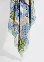The tropical silk scarf hanging in long folds showing palm and monstera leaves