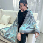 Woman on a cream sofa wearing the pale blue and grey horse print shawl open over a black top