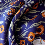 Close-up of navy silk folds printed with orange blooms and slender sage leaves