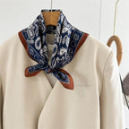 Navy paisley square tied at the throat of a cream blazer, rust edging framing the knot