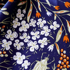 Macro of white blossom clusters, orange buds and a small beetle on navy charmeuse