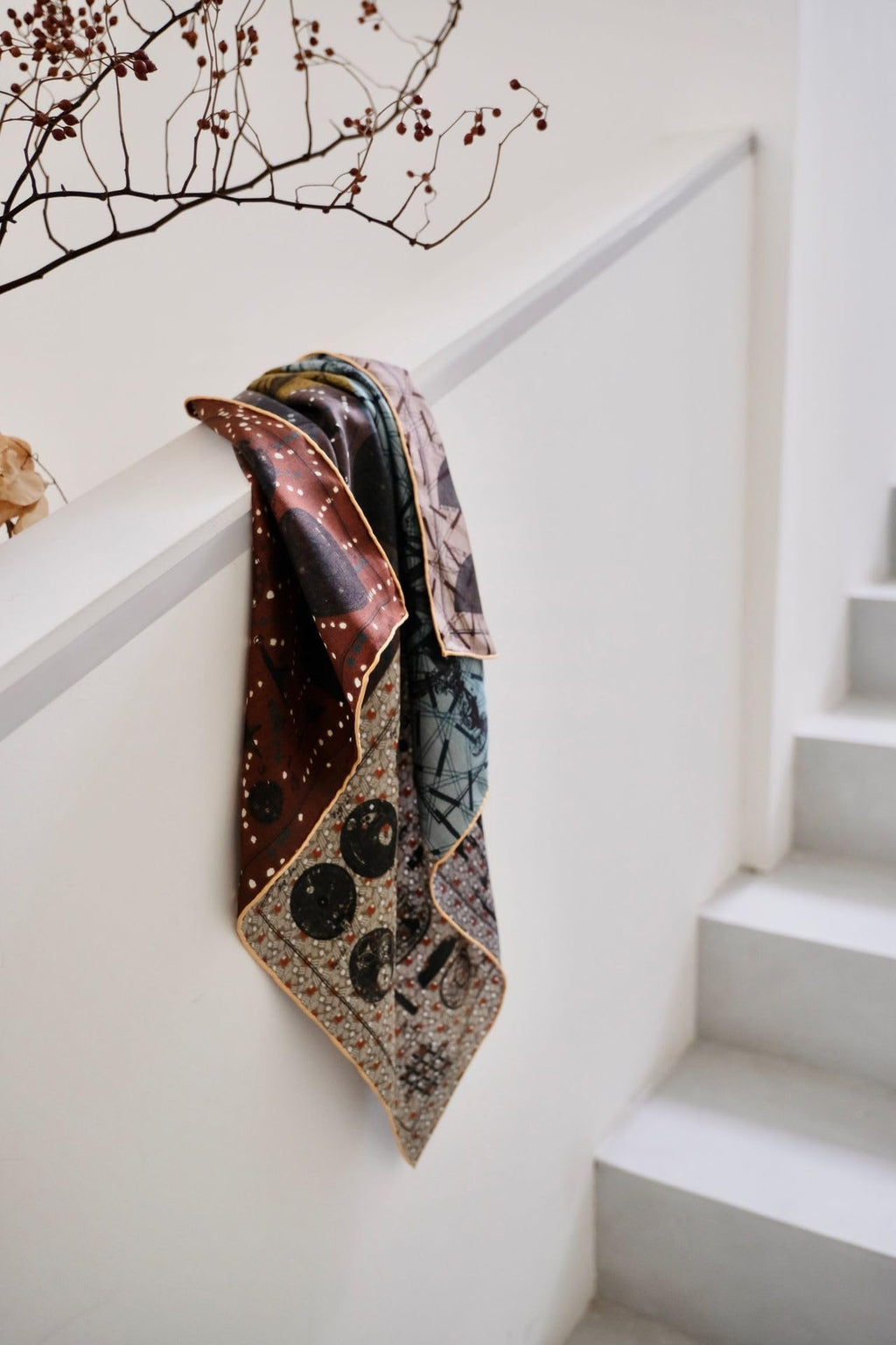 Astronomy print silk neckerchief draped over a white stair rail showing the oxblood star field and gold rolled hem