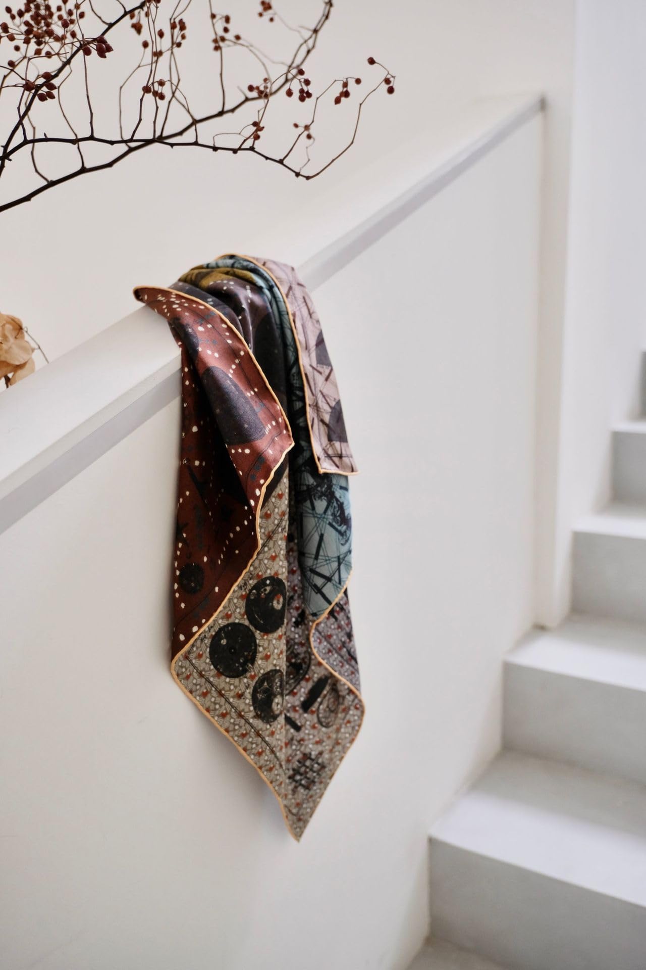 Astronomy print silk neckerchief draped over a white stair rail showing the oxblood star field and gold rolled hem