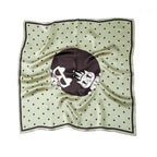 Sage green silk square with black dots and a dark medallion holding two cartoon cats