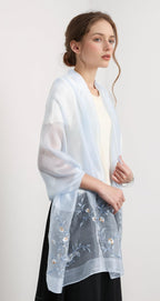 Model wearing the pale blue shawl open over a cream top and black skirt