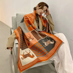 Woman seated in a pale armchair with the orange horse print shawl over her shoulders and across her lap