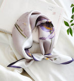 Mauve iris square coiled and knotted beside an open book and green leaves
