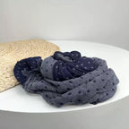 Jeelow reversed dot scarf bundled loosely on a white table beside a straw hat, the grey half with navy dots facing up