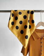 Golden yellow silk square with brushed black dots hung on a rail beside a mustard shirt