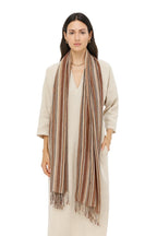 Woman in a cream dress wearing the striped cotton linen scarf draped long over both shoulders