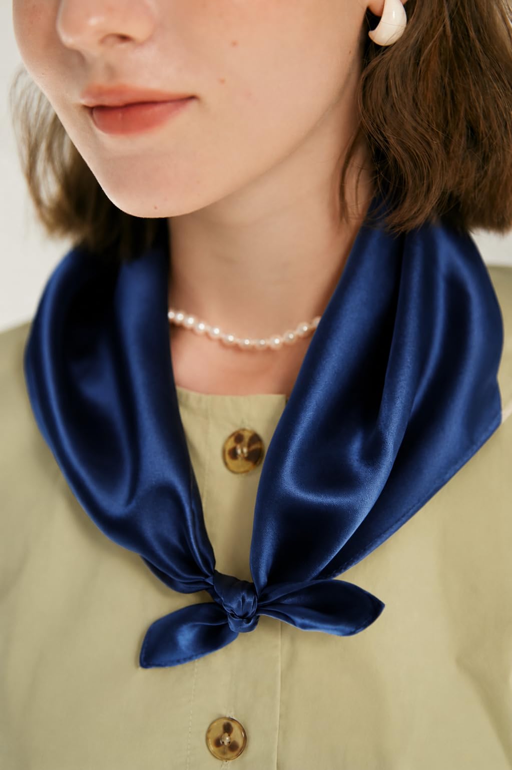 Model in a sage shirt and pearl necklace, navy silk square knotted at the neck