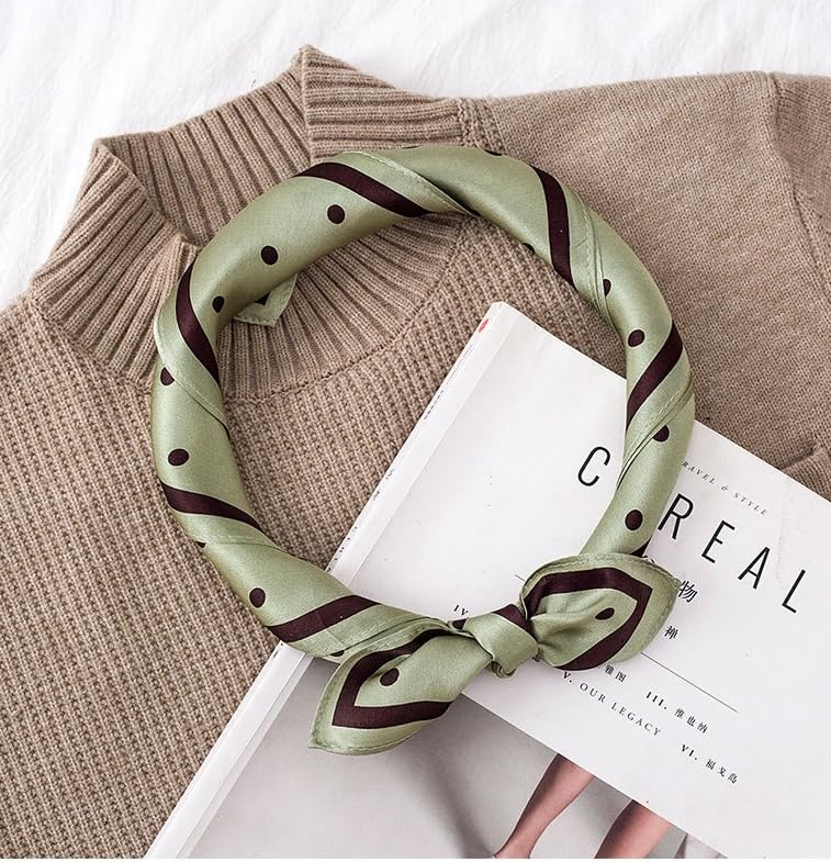 Sage green dotted silk rolled into a loop, resting on a camel knit sweater and a magazine