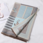 Folded pale blue shawl on white linen beside a magazine showing the grid and stripe panels