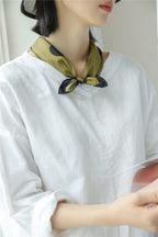 Olive dotted scarf tied snug at the neck over a loose white linen top
