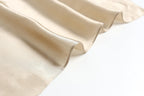 Champagne beige silk falling in even ripples, hemmed edge catching the light