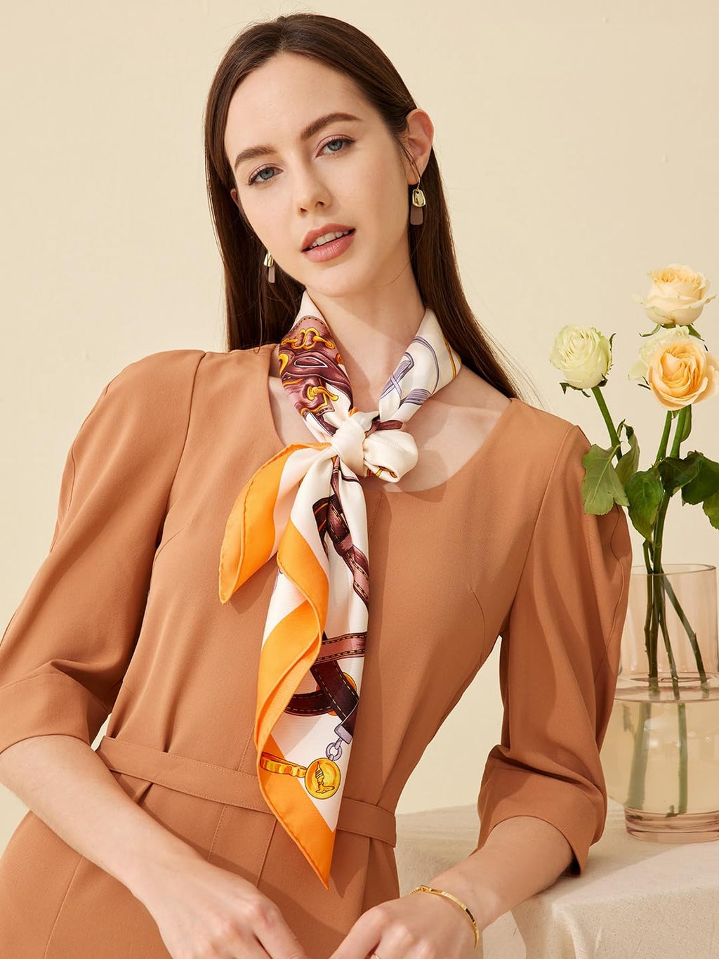Cream and orange equestrian silk scarf tied at the neck beside a vase of roses