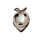 Greige silk square with black dots coiled at a white bust, bow tied at the top