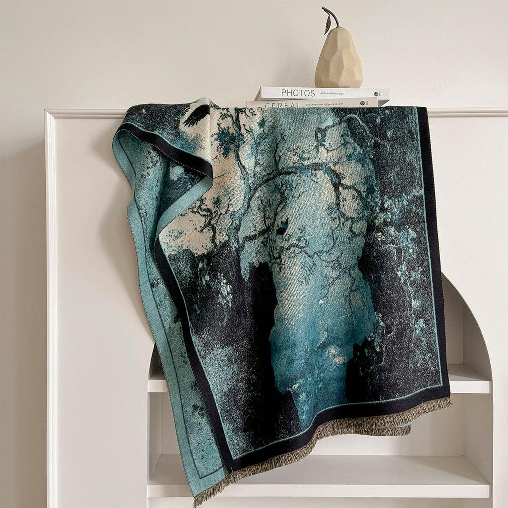 The marbled teal shawl laid over a white shelf showing the ink wash pooling into pale mist and the black edge