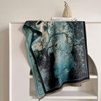 The marbled teal shawl laid over a white shelf showing the ink wash pooling into pale mist and the black edge