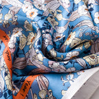 Close-up of blue silk in soft folds, white blooms beside the orange border band