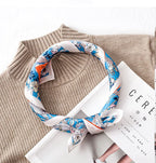 The same blue floral square rolled into a loose collar loop and knotted on a beige ribbed knit