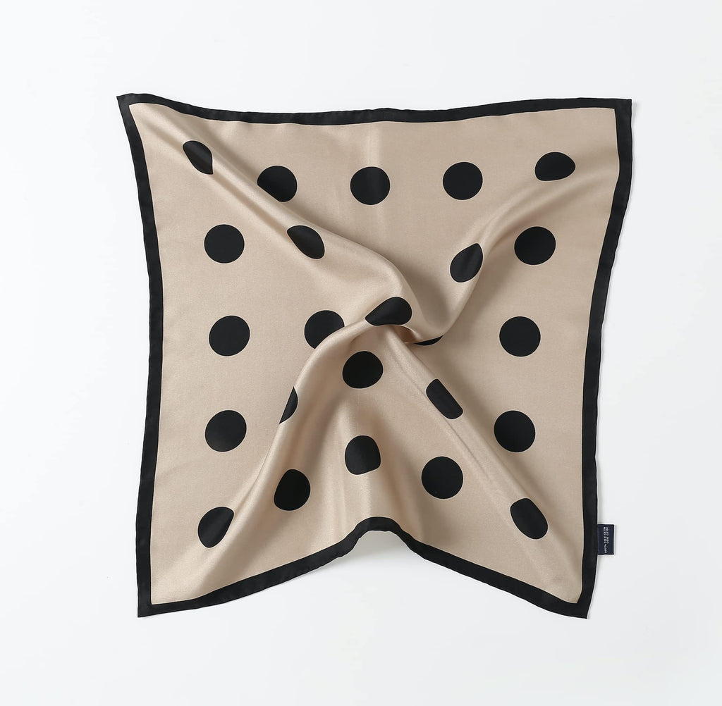 Greige silk square laid flat with a twisted centre, black dots inside a black border