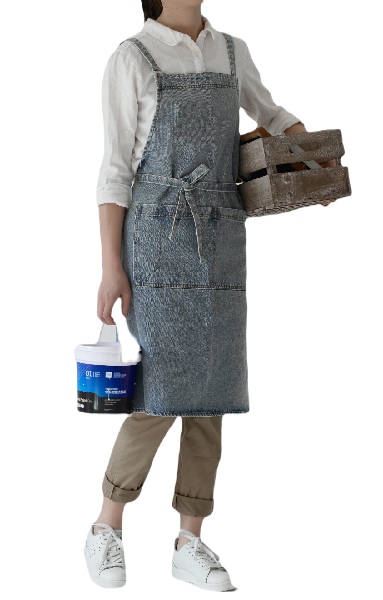 Woman in a pale stone washed denim cross back apron carrying a wooden crate