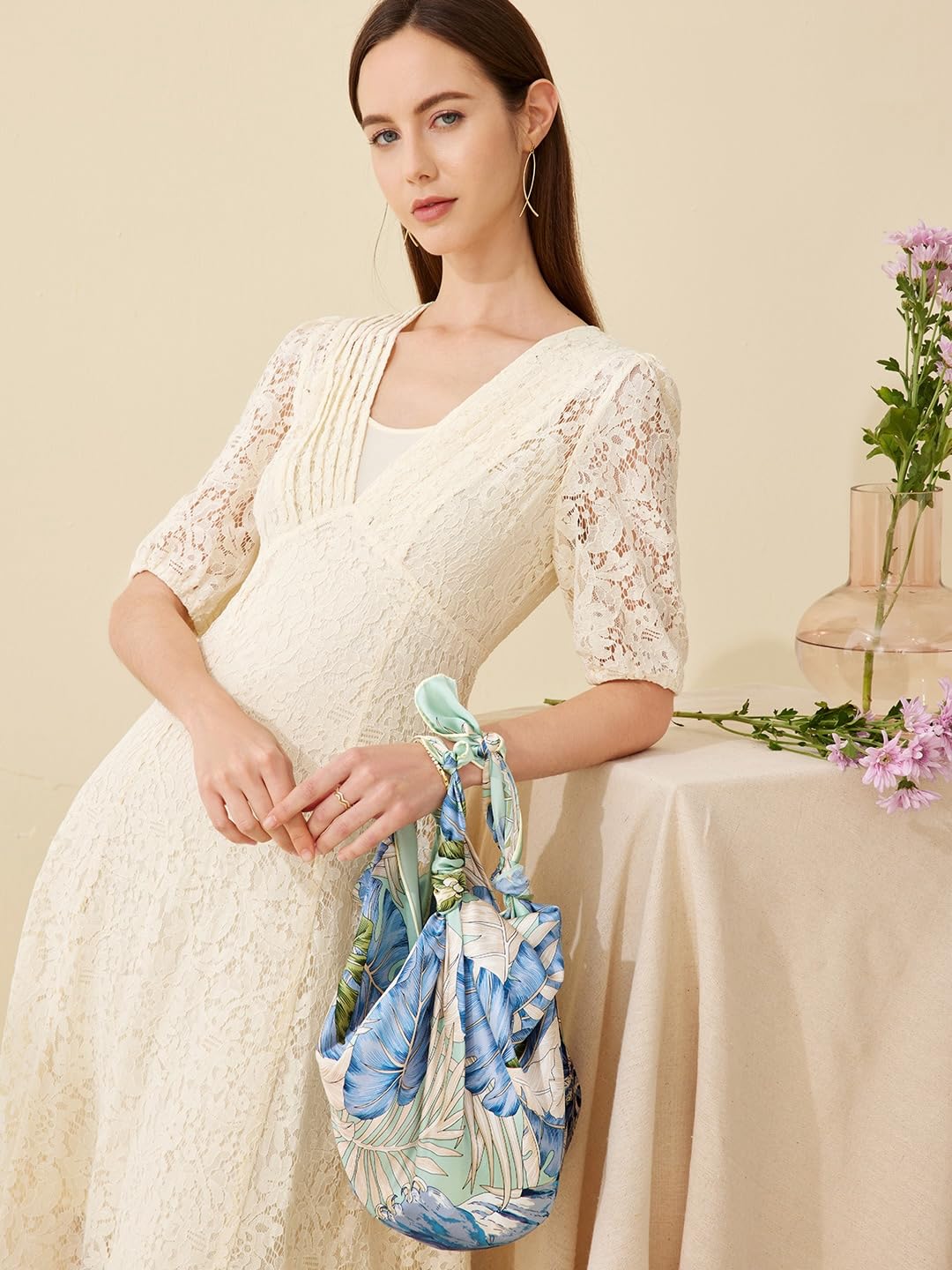 The hibiscus silk scarf knotted into a small pouch bag beside a vase of flowers