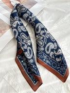 Navy paisley square twisted into a band on white linen, rust-tipped corner showing