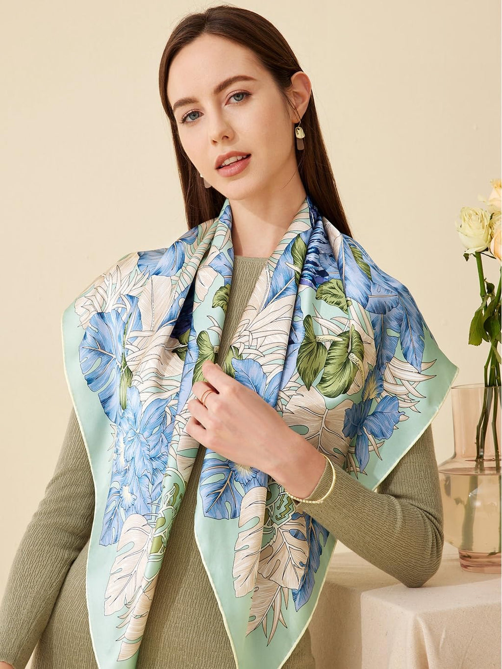 Model in olive knitwear wearing the blue hibiscus and palm print silk scarf draped wide
