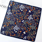 Navy square laid flat, orange blooms and white blossom over sage leaves and berries