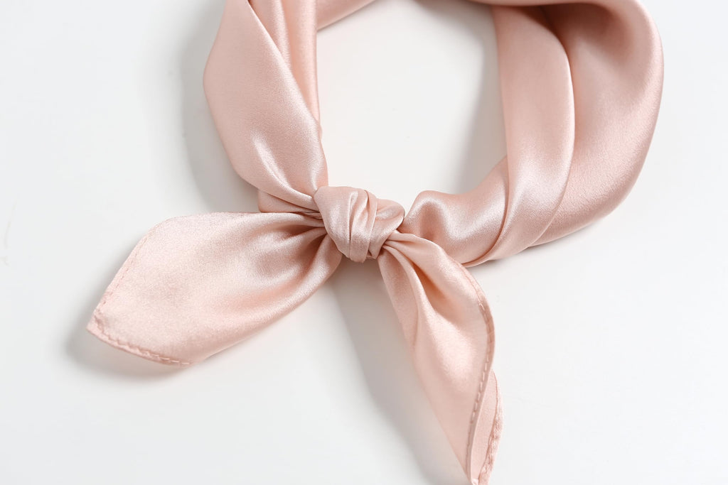 Close-up of a blush pink silk square knotted into a small bow, rolled hem in view