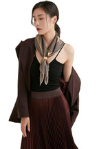 Woman in a brown blazer wearing a brown and cream houndstooth silk neckerchief with a gold saddle chain border