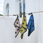Greige, olive and steel blue dotted silk squares knotted on a bamboo pole by a white wall