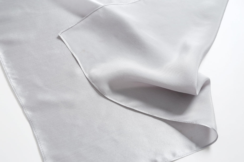 Cloud grey silk folded back on itself, hemmed corner and softer matte reverse in view
