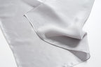 Cloud grey silk folded back on itself, hemmed corner and softer matte reverse in view