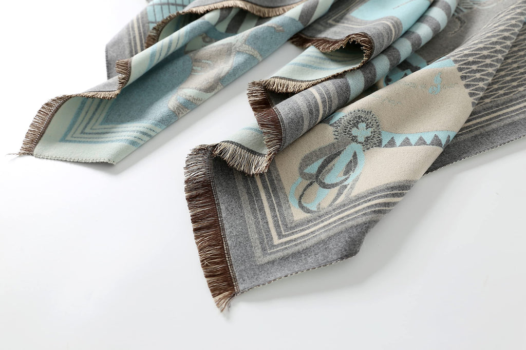 The pale blue shawl laid out in a loose S shape showing the brown fringe along both ends