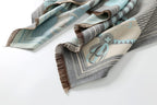 The pale blue shawl laid out in a loose S shape showing the brown fringe along both ends