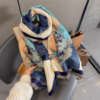 Hand holding the shawl loosely coiled on a grey chair showing the jade and ochre fans and the fringed ends