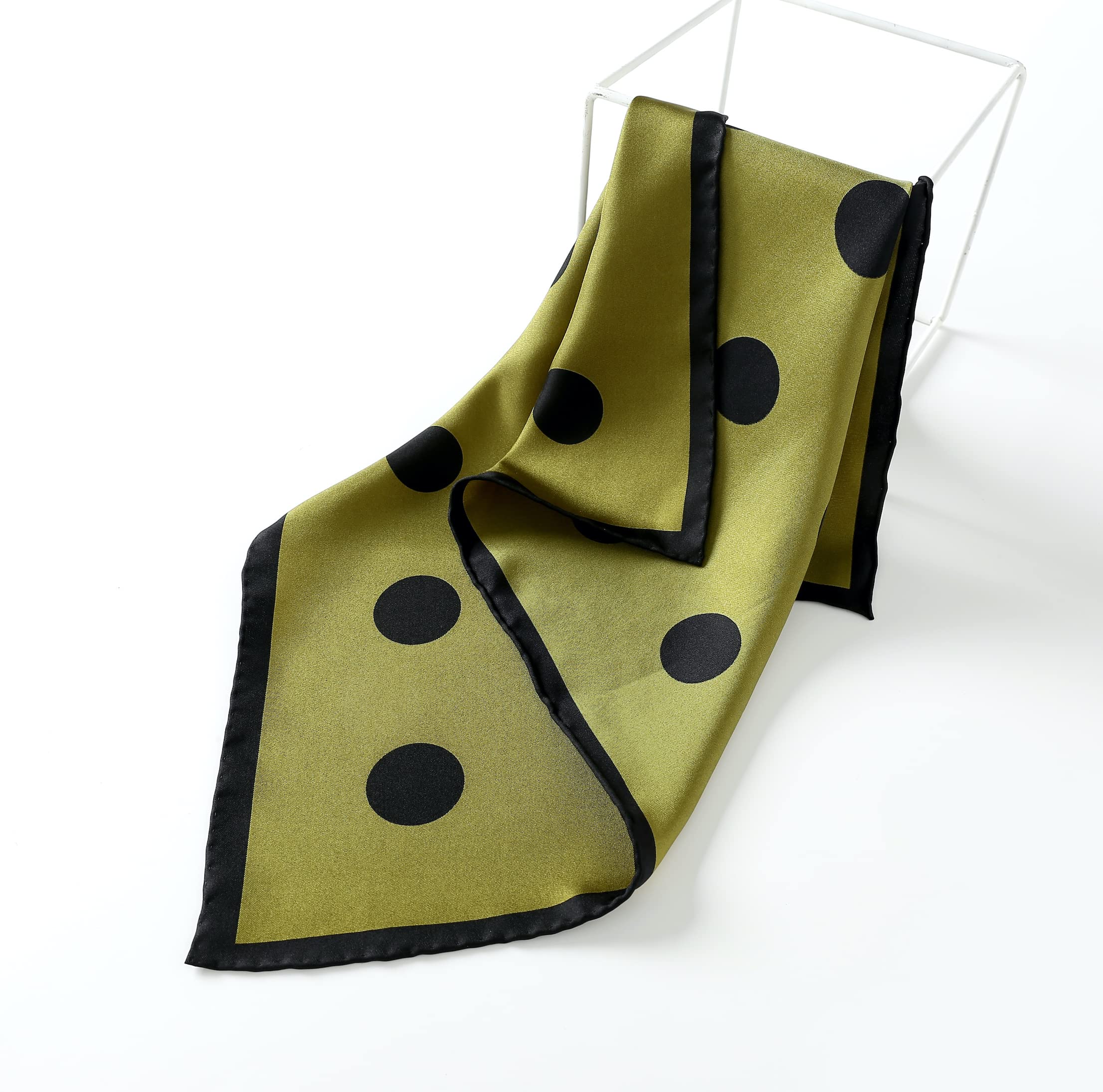 Olive dotted silk square draped over a white wire stool, black hemmed edge folding down