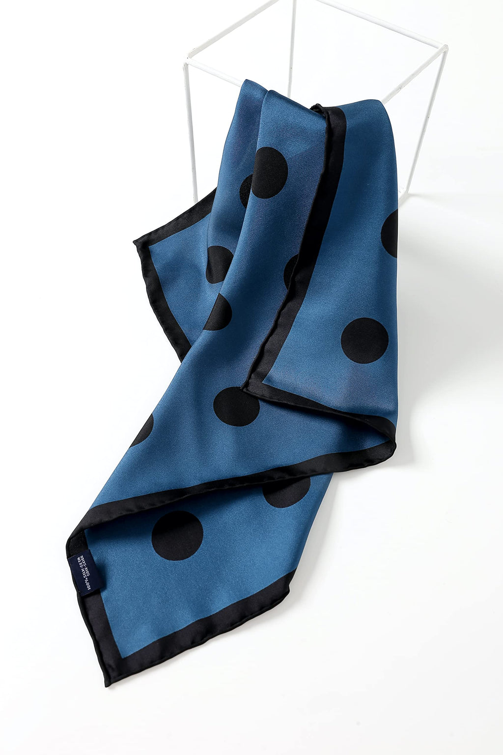 Steel blue polka dot square folded over a white wire stool, woven label at the lower corner