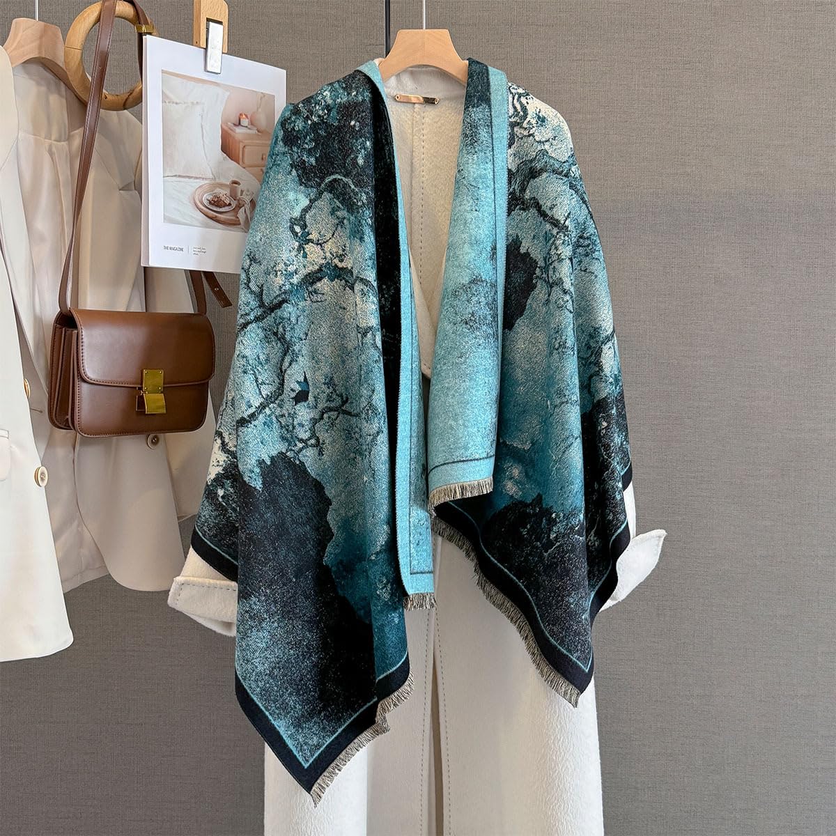 Marbled ink shawl hung open on a rail beside a cream coat and a tan leather bag