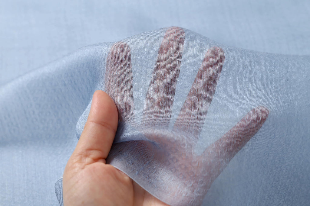 Hand held behind the denim blue fabric showing how sheer the ground is