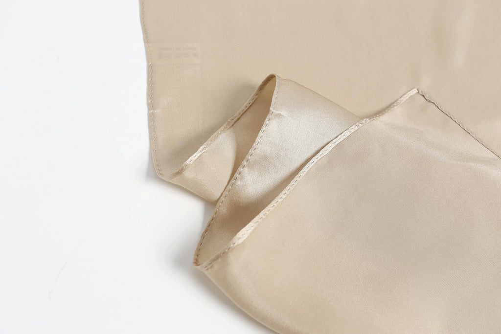 Champagne beige silk lifted at the edge, showing the narrow rolled hem and care label